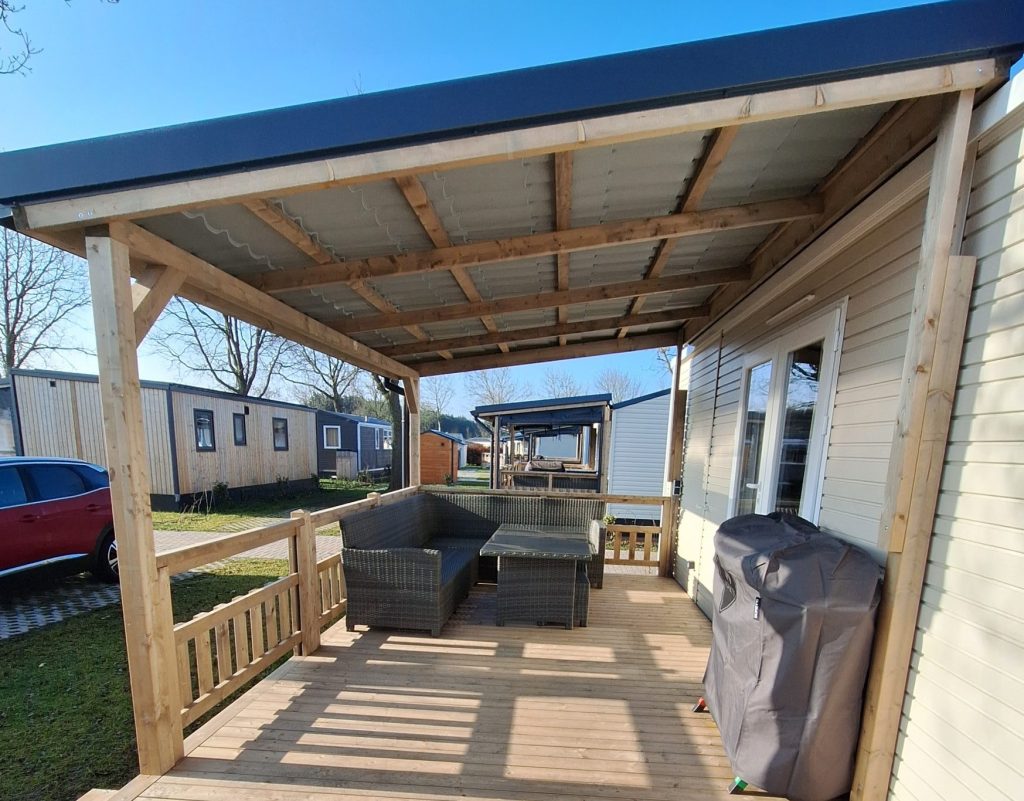 Eine Holzterrasse mit Sitzbereich, Gartenmöbeln und Grünpflanzen im Hintergrund.